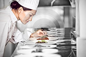 Concentrated female chef garnishing food in kitchen