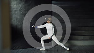 Concentrated fencer woman practice fencing exercises using VR headset and training simulator competition game indoors
