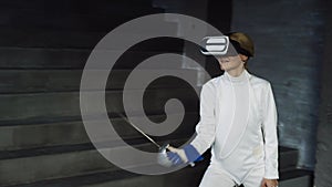 Concentrated fencer woman practice fencing exercises using VR headset and training simulator competition game indoors