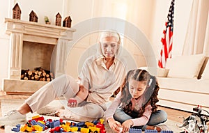 Concentrated girl and her grandmother playing with building blocks
