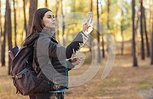 Concentrated girl standing in woods with smartphone