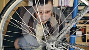 Concentrated guy skilled mechanic is repairing bicycle wheel with wrenchwhile working in his workplace. Bike maintenance