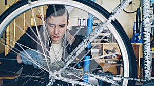 Concentrated guy skilled mechanic is repairing bicycle wheel with wrenchwhile working in his workplace. Bike maintenance