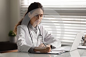 Concentrated hispanic female therapist sit at desk prepare medical report