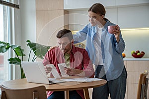 Concentrated husband holding bills, counting expenses, planning family budget on laptop computer