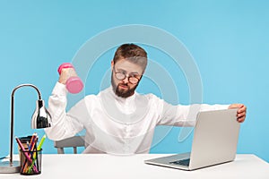 Concentrated intelligent man office worker in white shirt and eyeglasses doing sports exercises with dumbbell watching lesson at