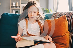 Concentrated kid girl reading interesting book at home