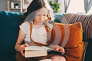 Concentrated kid girl reading interesting book at home