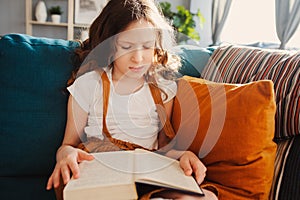 Concentrated kid girl reading interesting book at home