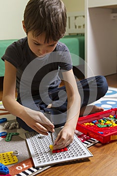 Concentrated kid playing with toys construction tool kit while sitting on the floor in his room