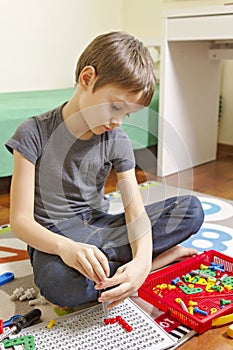 Concentrated kid playing with toys tool kit while sitting on the floor in his room