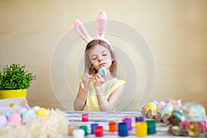 Concentrated little girl in bunny ears painting Easter eggs at home prepares to Easter. Happy easter