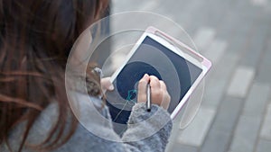 Concentrated little girl drawing stick figures on a tablet