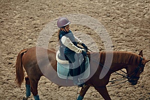 Concentrated little girl in inform and special clothes siting on horse, training horseback riding on special manege
