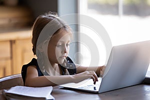 Concentrated little girl studying online doing homework on laptop