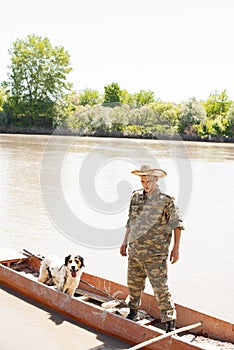 Concentrated male angler with faithful dog standing in boat, mooring after fishing in countryside.