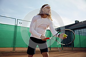 Concentrated male tennis player with racket and ball training on outdoor court