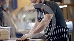 Concentrated man in apron and Covid face mask cutting cooked roasted meat on restaurant kitchen in slow motion