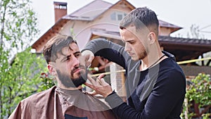 Concentrated man doing his beard at home in the garden professional barber man take the scissors and cut the hair form