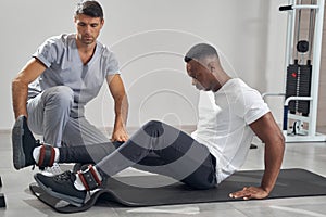 Concentrated man foam-rolling his calf muscles supervised by physiotherapist