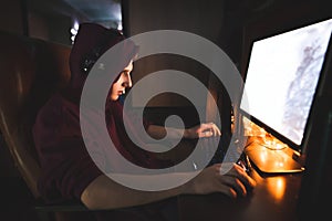 Concentrated man in his hood sits at night at the computer and plays video games