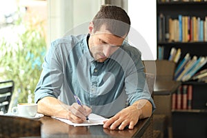 Concentrated man writing notes in a paper in a coffee shop