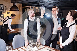 Concentrated manager checking wineglass while waiters serving ta