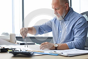 Concentrated mature business man working with drawing compass while sitting in the modern working space