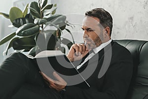 concentrated mature businessman reading book while sitting