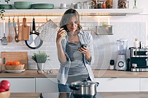 Concentrated mature woman using her mobile phone while drinking a cup of coffee at home