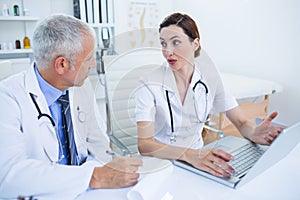 Concentrated medical colleagues discussing and working with laptop