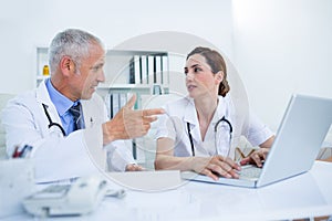 Concentrated medical colleagues discussing and working with laptop