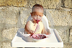 Concentrated messy baby boy eating blueberry cake