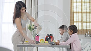 Concentrated Middle Eastern woman pouring smoothie in glass preparing healthful fruit drink for children in kitchen. Son