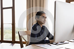 Concentrated millennial Indian businesswoman working online in office.