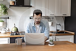 Concentrated millennial male engaged in telework from home using laptop