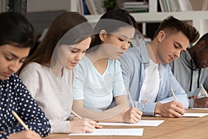 Concentrated mixed race students passing evaluation examination during session.