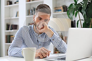 Concentrated modern business man analyzing data using laptop while working in the office