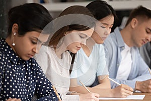 Concentrated multiethnic students busy writing test in classroom