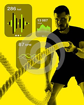 Concentrated muscular man training with rope against monochrome yellow background with fitness tracking app element