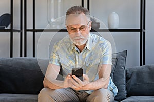 Concentrated old retired man using cellphone at home.