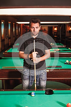 Concentrated player with a cue in billiard room.