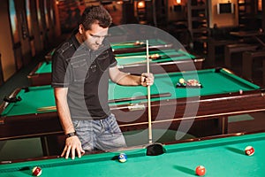 Concentrated player with a cue in billiard room.