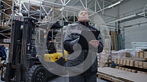 Concentrated professional warehouse worker filling in bill of lading standing in industrial storage indoors writing with