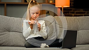 Concentrated pupil girl making homework at copybook on cosy sofa writing math tasks of elementary school subjects
