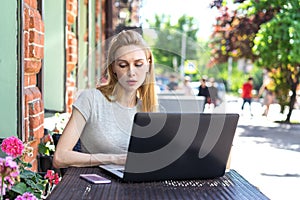 A concentrated Self employed Caucasian woman working with her phone and laptop in a restaurant terrace