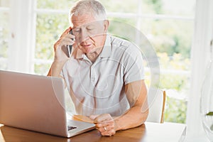 Concentrated senior man looking at laptop and phone calling