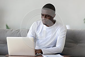 Concentrated serious millennial african american guy working with laptop.