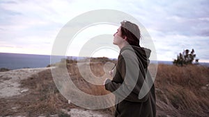 Concentrated slim woman jogging on a cliff above the sea at sunset in cloudy weather. Endurance training, preparation