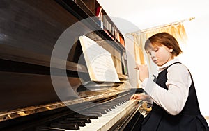 Concentrated small girl in uniform playing piano